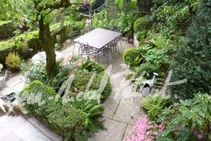 Jardin avec végétation dense et dallage en pierres anciennes